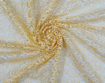 May include: A sheer, pale yellow lace fabric featuring a repeating floral and vine pattern. The material is gathered in the center, creating a spiral effect that highlights the intricate, openwork design and the delicate, lightweight texture.