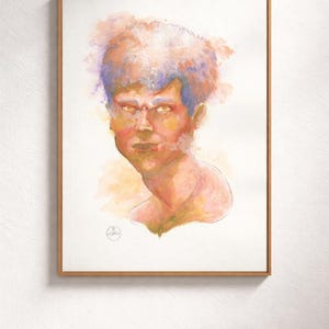 May include: Watercolor portrait of a person with orange, yellow, and purple hues. The artwork is framed in a light brown wooden frame and is set against a white wall. The subject's expression is intense.