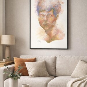 May include: A framed watercolor portrait of a person with blue and orange hair. The artwork is displayed above a light-colored sofa with decorative pillows. A wooden coffee table and a lamp are in the foreground.