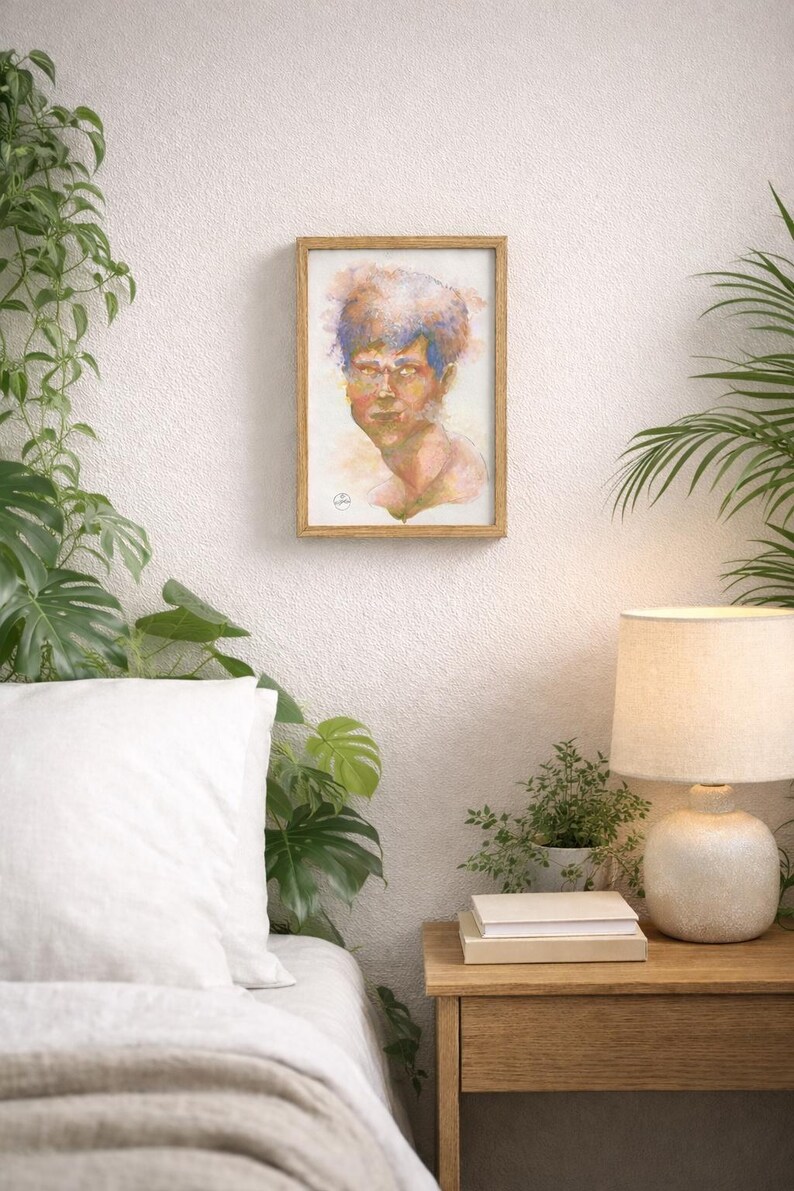 May include: A framed watercolor portrait of a person with blue and orange hair. The artwork is displayed on a white wall, surrounded by greenery and a bedside table with a lamp and books.