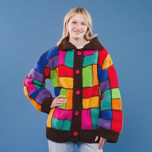 Op de afbeelding: Een gehaakt vest met lange mouwen en een levendig patchworkpatroon van rechthoekige blokken in rood, oranje, geel, groen, blauw en paars. Het kledingstuk heeft een donkerbruine kraag, boorden, zoom en een knoopsluiting met vijf felroze knopen.