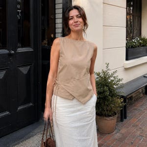 May include: A sleeveless beige wrap top featuring a side tie closure with thin fabric strings and a straight neckline, paired with a long, flowing white skirt. The top has an asymmetrical hemline that overlaps at the front waist area.