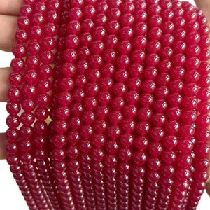 May include: A collection of smooth, round, vibrant red beads arranged in multiple vertical strands. Each bead features a polished, glossy finish that reflects light, creating a uniform appearance across the entire set of circular jewelry components.