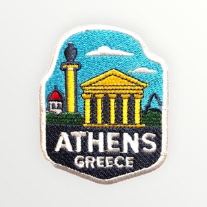 Puede incluir: Parche bordado que representa Atenas, Grecia. El diseño incluye un edificio amarillo, una columna alta amarilla y el texto "ATHENS GREECE" en blanco. El parche tiene un fondo de cielo azul con nubes blancas.