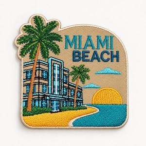 May include: An embroidered patch featuring a tan background with the text MIAMI BEACH in teal and blue. The design includes a multi-storey building, two green palm trees, a yellow sun, and a blue ocean shoreline with a sandy yellow beach area.
