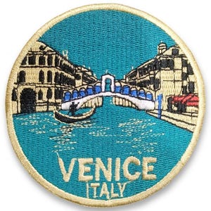 May include: Embroidered patch featuring a teal background with a detailed depiction of Venice, Italy. The design includes buildings, a bridge, a gondola, and the text "VENICE ITALY" in gold lettering, surrounded by a gold border.