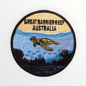 May include: Circular embroidered patch depicting a turtle in the ocean. The patch features the text "GREAT BARRIER REEF AUSTRALIA". The design includes a turtle, water, and reef elements, with a black border.