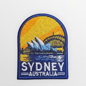 May include: Embroidered patch depicting the Sydney Opera House and Harbour Bridge set against a yellow and orange sunset. The patch is edged in blue and features the text "SYDNEY AUSTRALIA" in white.
