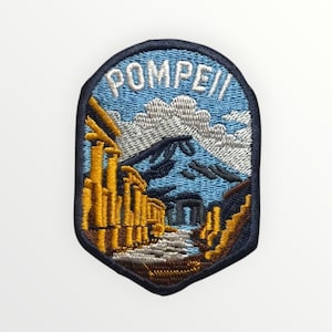 May include: Embroidered patch with the word "POMPEII" above a landscape scene. The design features yellow structures, a mountain, and clouds, set against a blue sky and a dark blue border.