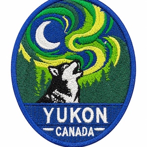 Peut inclure: Un écusson brodé ovale représentant un loup noir et blanc hurlant vers un croissant de lune blanc sur fond vert foncé avec des motifs d'aurores boréales jaunes et vertes. Le texte YUKON CANADA est brodé en lettres blanches.