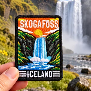 May include: A rectangular embroidered patch featuring a colorful landscape of the Skogafoss waterfall in Iceland. The design includes a bright yellow sun, orange sky, green hills, and a blue waterfall with white text reading SKOGAFOSS and ICELAND.