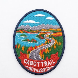 Könnte beinhalten: Ovaler, gestickter Aufnäher mit einer malerischen Landschaft mit einer kurvenreichen Straße, Bergen und einem See. Der Aufnäher hat einen blauen Rand und den Text "CABOT TRAIL NOVA SCOTIA" in Weiß auf einem roten Banner. Der Himmel ist blau mit weißen Wolken.