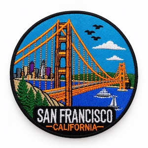 Puede incluir: Un parche bordado circular que muestra el puente Golden Gate en naranja sobre un cielo azul. El diseño incluye árboles verdes, un horizonte urbano, nubes blancas, pájaros y barcos en el agua. El texto dice SAN FRANCISCO CALIFORNIA.