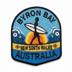 Puede incluir: Parche bordado con la silueta de un surfista caminando con una tabla de surf, contra un atardecer. El parche dice "BYRON BAY" encima del surfista, y "NEW SOUTH WALES AUSTRALIA" debajo, con colores azul, naranja y negro.