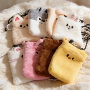 May include: A collection of plush, animal-shaped phone pouches in various colors, including pink, brown, yellow, and white. Each pouch features a different animal face, such as a cat, wolf, and bunny, with a black and white cord strap.