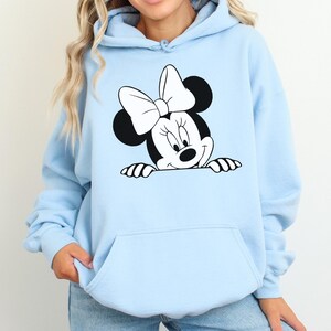 May include: Light blue hoodie featuring a black and white Minnie Mouse graphic. The graphic shows Minnie Mouse's face, bow, and hands. The hoodie has a front pocket and a drawstring hood.