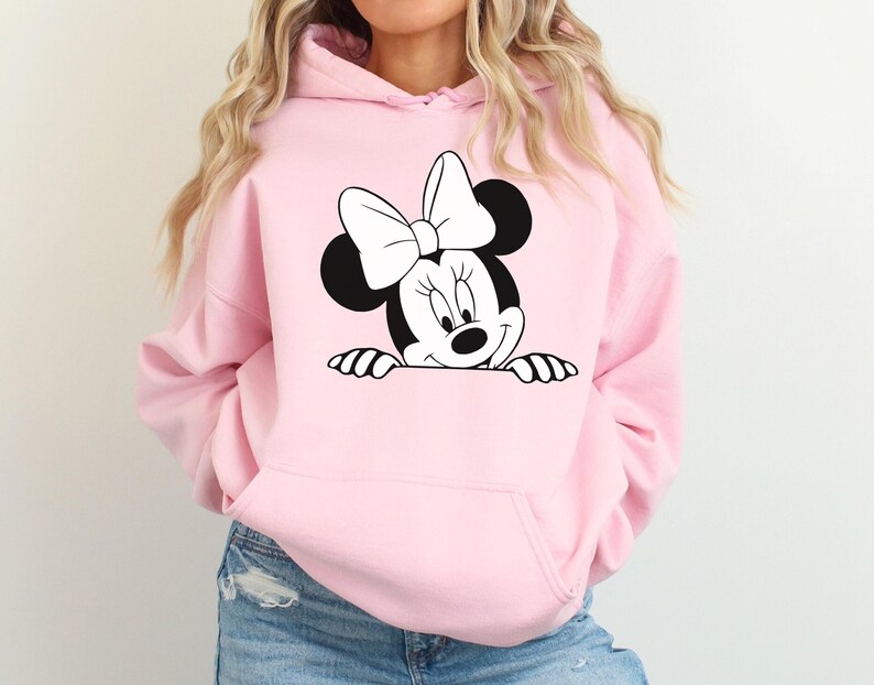 May include: Light pink hooded sweatshirt featuring a black and white Minnie Mouse graphic. The graphic shows Minnie Mouse peeking over the bottom edge of the sweatshirt. The sweatshirt has a front pocket and a drawstring hood. The sleeves are long.