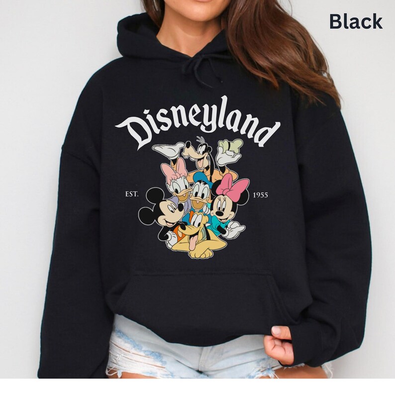 May include: Black hooded sweatshirt featuring the word "Disneyland" in white script above a graphic of Mickey Mouse, Minnie Mouse, Donald Duck, Daisy Duck, Goofy, and Pluto. The text "EST. 1955" is below the graphic.