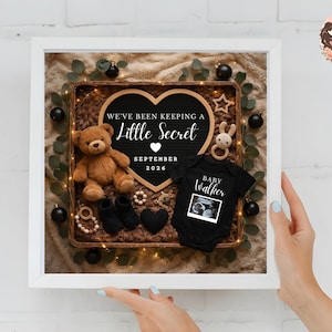 Pu&ograve; includere: Annuncio incorniciato con un cartello a forma di cuore che recita "We've Been Keeping a Little Secret September 2026". Il display include un orsacchiotto, vestiti per bambini, stivaletti e un'immagine ecografica. La cornice &egrave; bianca.