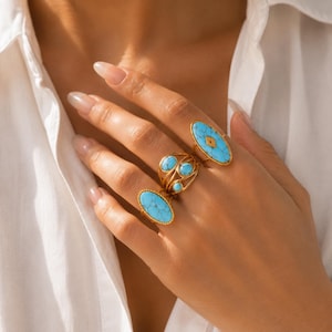 May include: Three gold-toned rings featuring bright blue turquoise-colored stones with dark veining. One ring has a large oval stone, another has a smaller oval stone, and the center ring features three small round stones set in a wire-like band.