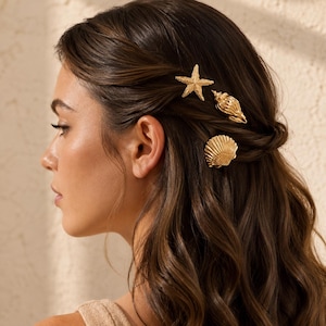 May include: A set of three gold-toned hair clips featuring a textured starfish, a spiral conch shell, and a fan-shaped scallop shell. These metallic hair accessories are secured into wavy brown hair, showcasing detailed nautical designs.