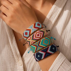 May include: A set of four woven friendship bracelets featuring intricate geometric diamond patterns in vibrant colors including light blue, red, orange, white, teal, and dark navy blue, each finished with adjustable thin cord ties at the ends.