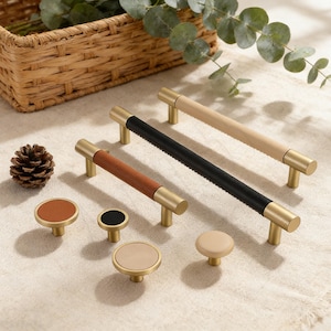 May include: A collection of cabinet hardware, including brass-toned handles with brown, black, and natural wood accents, and matching knobs. The handles vary in length. A pinecone and a woven basket are in the background.