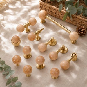 May include: A collection of wooden and brass cabinet hardware, including knobs and pulls. The knobs are spherical with a light wood grain, and the pulls have a brass finish. The hardware is arranged on a neutral-toned surface.