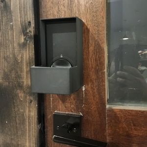 May include: A black smart lock and door handle set installed on a wooden door. The smart lock has a rectangular housing and a circular keypad. The door handle is a simple, modern design.