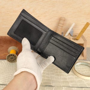 Puede incluir: Una cartera negra plegable que presenta una ventana rectangular de malla para identificaci&oacute;n en el lado izquierdo y m&uacute;ltiples ranuras horizontales para tarjetas en el lado derecho. La cartera tiene bordes cosidos y una superficie interior lisa.
