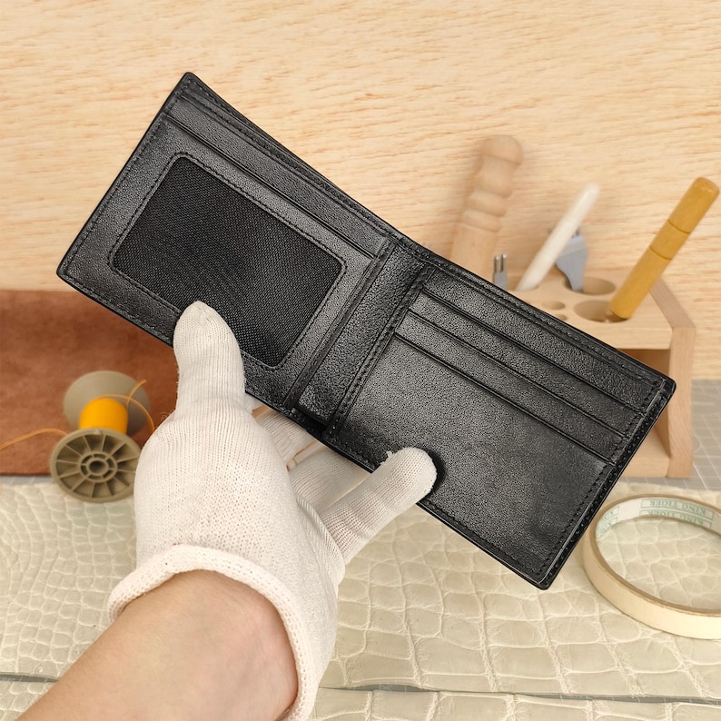 Puede incluir: Una cartera negra plegable que presenta una ventana rectangular de malla para identificaci&oacute;n en el lado izquierdo y m&uacute;ltiples ranuras horizontales para tarjetas en el lado derecho. La cartera tiene bordes cosidos y una superficie interior lisa.