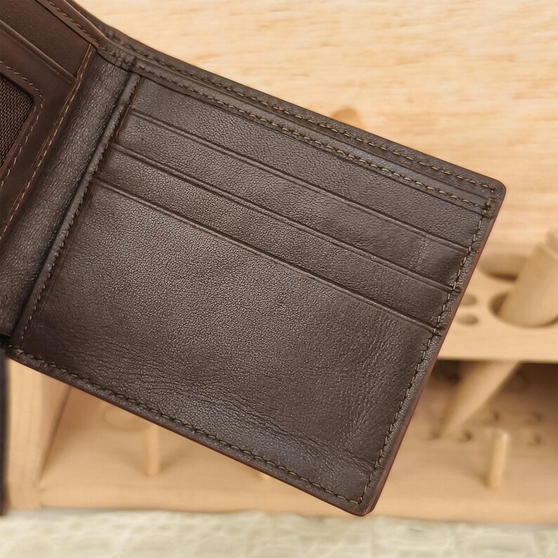 Puede incluir: Una cartera bifold de color marr&oacute;n oscuro que presenta m&uacute;ltiples ranuras horizontales para tarjetas en el panel interior. La cartera est&aacute; construida con costuras tonales visibles a lo largo de los bordes y compartimentos, con una textura mate.