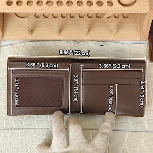 Puede incluir: Una cartera bifold de cuero marr&oacute;n con una ventana transparente para identificaci&oacute;n y m&uacute;ltiples ranuras para tarjetas. La cartera mide 22 cm de ancho por 9 cm de alto abierta, con secciones internas de 9,3 cm por 7,8 cm y 6,9 cm por 4,8 cm.