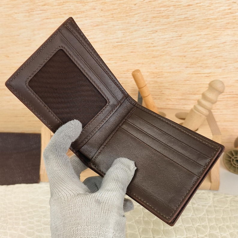 Puede incluir: Una cartera plegable de color marr&oacute;n oscuro que presenta una ventana transparente para identificaci&oacute;n en el lado izquierdo y varias ranuras horizontales para tarjetas en el lado derecho, con costuras visibles en los bordes.