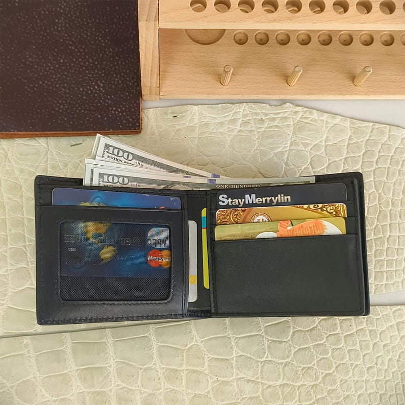 Puede incluir: Una cartera negra plegable con una ventana transparente para identificaci&oacute;n en el lado izquierdo que contiene una tarjeta con un gr&aacute;fico de globo terr&aacute;queo, y varias ranuras en el lado derecho con tarjetas, incluyendo una con StayMerrylin y billetes.