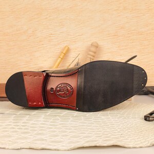 May include: Close-up of the sole of a black leather shoe with a Goodyear logo. The sole is black with a brown heel and a Goodyear logo. The shoe is on a white surface.