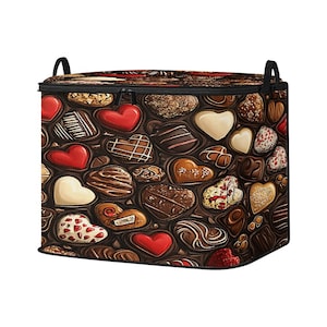 Könnte beinhalten: Eine rechteckige Aufbewahrungsbox mit Reißverschluss und schwarzen Griffen. Die Außenseite der Box zeigt ein sich wiederholendes Muster von herzförmigen Pralinen in verschiedenen Farben und Designs, darunter Rot, Weiß und Braun.