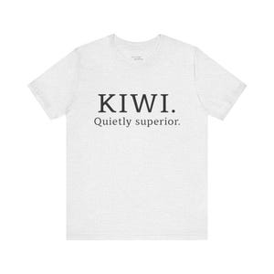 Peut inclure: Un t-shirt gris clair avec le mot "KIWI" en gras, en noir, suivi de "Quietly superior." en plus petit, en noir. Le t-shirt est fait d'une matière douce.