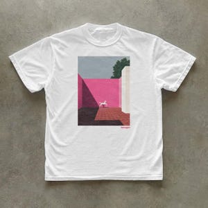 May include: A white short-sleeve t-shirt featuring a rectangular graphic print of a courtyard with a bright pink wall, a white horse figure, and deep shadows. The text "barragán" is printed in small pink letters below the graphic.