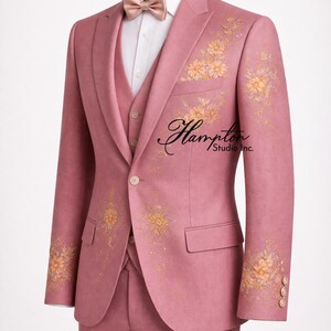 K&ouml;nnte beinhalten: Ein rosa Anzug mit floraler Stickerei, bestehend aus Blazer, Weste und Hose. Der Blazer hat goldene Blumenmuster auf den &Auml;rmeln und der Vorderseite. Eine Fliege und ein wei&szlig;es Hemd vervollst&auml;ndigen das Ensemble. Der Anzug hat den Text "Hampton Studio Inc."