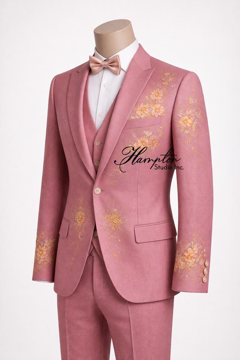 K&ouml;nnte beinhalten: Ein rosa Anzug mit floraler Stickerei, bestehend aus Blazer, Weste und Hose. Der Blazer hat goldene Blumenmuster auf den &Auml;rmeln und der Vorderseite. Eine Fliege und ein wei&szlig;es Hemd vervollst&auml;ndigen das Ensemble. Der Anzug hat den Text "Hampton Studio Inc."