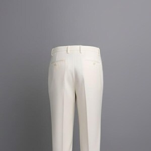 May include: Cream-colored dress pants with a tailored fit. The pants feature a classic design with a button and zipper closure, belt loops, and pockets. The fabric appears to be a smooth, woven material. The pants are displayed against a gray background.