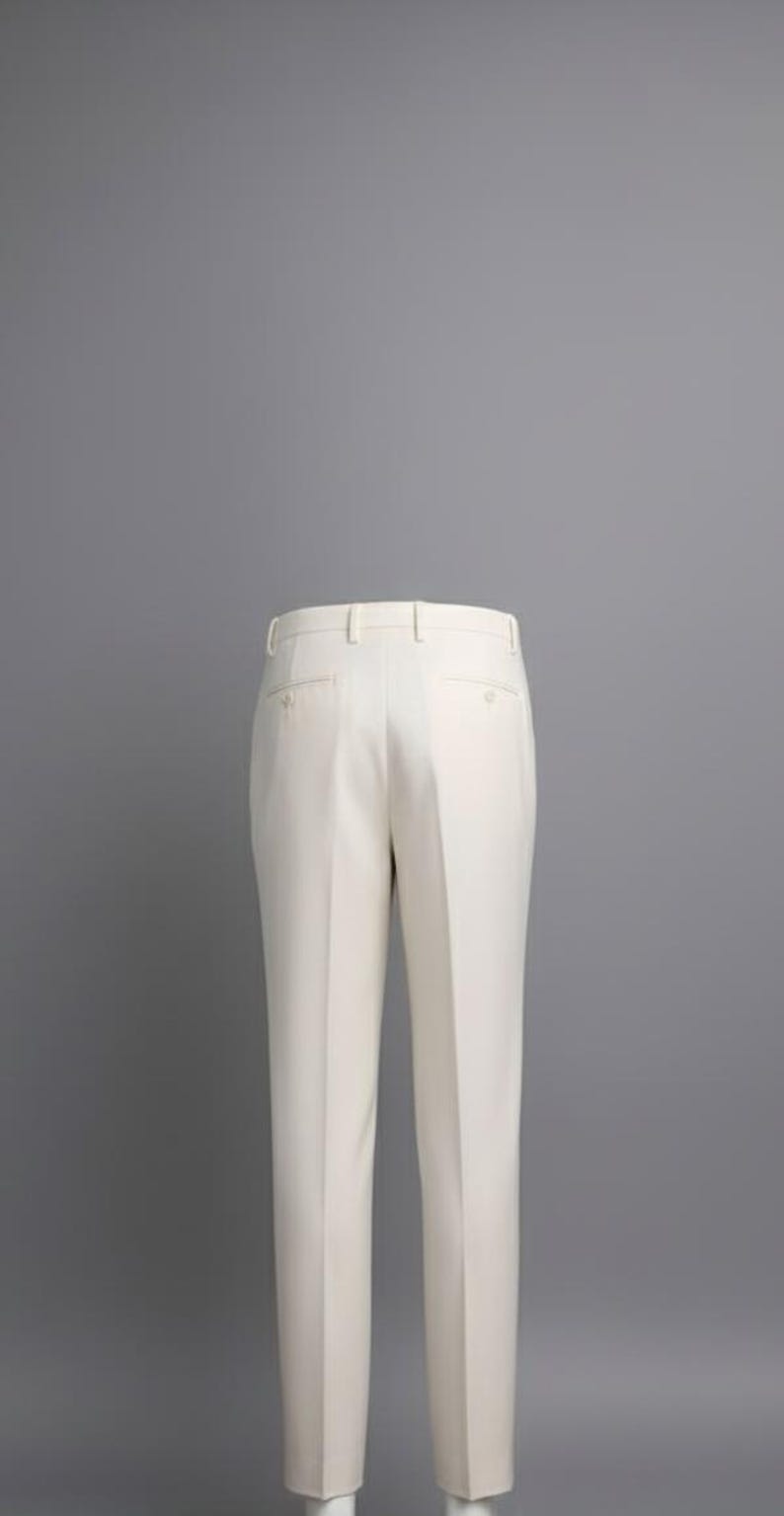 May include: Cream-colored dress pants with a tailored fit. The pants feature a classic design with a button and zipper closure, belt loops, and pockets. The fabric appears to be a smooth, woven material. The pants are displayed against a gray background.