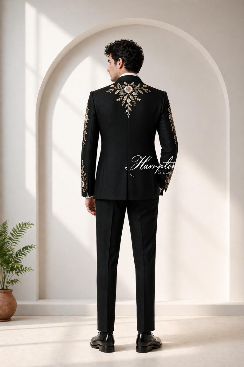 May include: Black suit with gold embroidery on the shoulders and sleeves. The suit includes a jacket and matching pants. The back of the jacket features an elaborate floral design. The suit is worn with a white collared shirt and black shoes. The text "Hampton Studios" is visible.