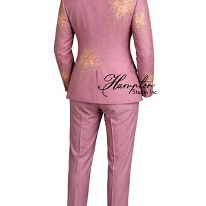 K&ouml;nnte beinhalten: Ein staubrosa Anzug mit floralen Stickereien an den &Auml;rmeln und am R&uuml;cken der Jacke. Der Anzug besteht aus einer Zweiknopfjacke und einer passenden Hose. Das Bild zeigt die R&uuml;ckseite des Anzugs mit dem Text "Hampton Studio Inc.".