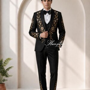 May include: A black tuxedo with gold floral embroidery. The suit includes a jacket, vest, and trousers. The jacket features floral designs on the shoulders and lapels. The trousers have matching floral accents. The outfit is completed with a bow tie and dress shoes.