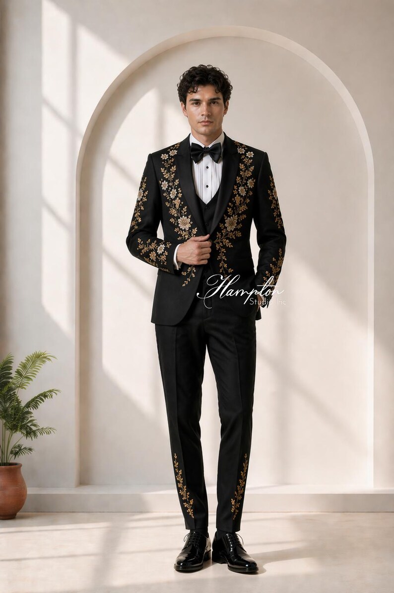 May include: A black tuxedo with gold floral embroidery. The suit includes a jacket, vest, and trousers. The jacket features floral designs on the shoulders and lapels. The trousers have matching floral accents. The outfit is completed with a bow tie and dress shoes.