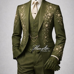 May include: Olive green three-piece suit with floral embroidery. The suit includes a jacket, vest, and trousers. The jacket features detailed floral embroidery with pearl accents. A gold chain and tie clip add a touch of elegance. The suit is displayed on a mannequin.