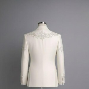 May include: Ivory-colored blazer with intricate silver embroidery on the shoulders and sleeves. The tailored jacket features a classic design with a two-button closure and a notched lapel. The back view showcases the detailed craftsmanship of the formal wear.