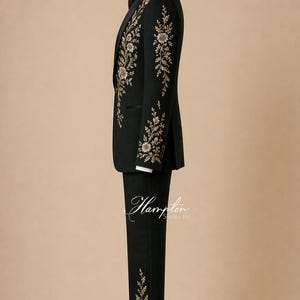 May include: A dark green suit with gold floral embroidery on the jacket and pants. The suit is displayed on a mannequin with a black bow tie and white dress shirt. The suit is a formal wear item.